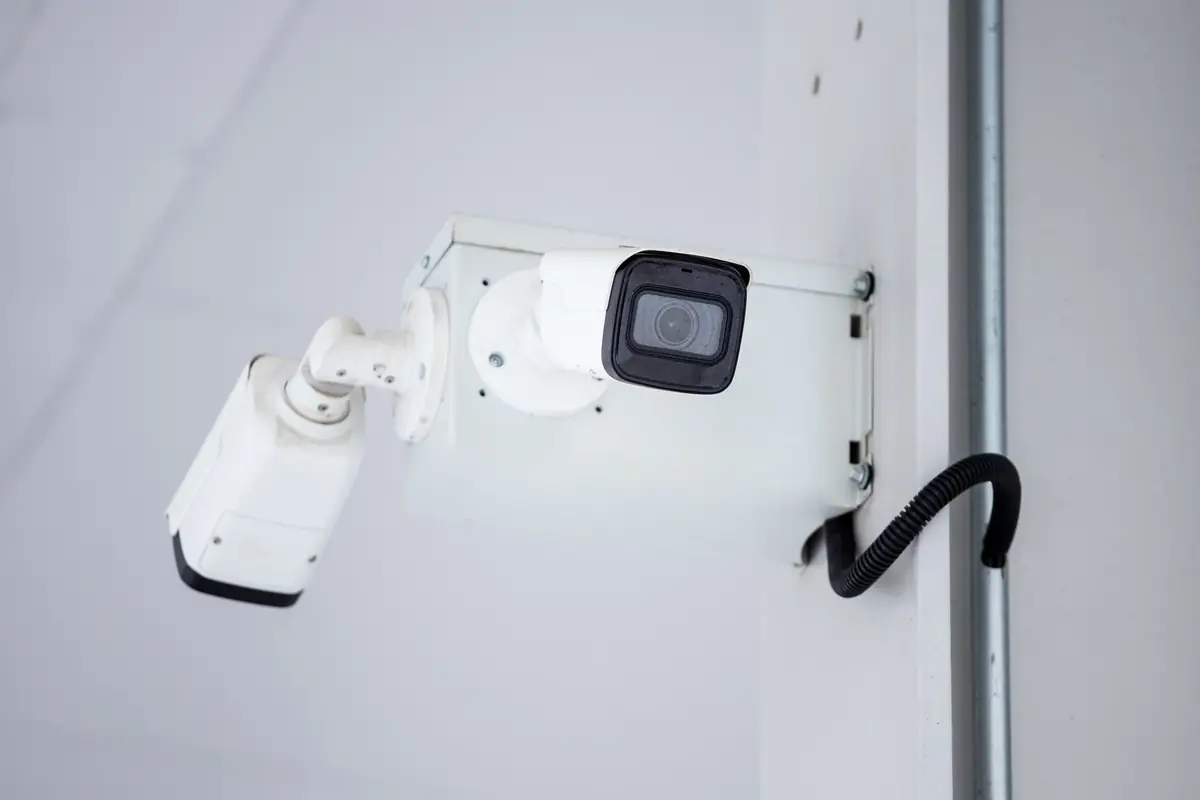 Une caméra de vidéosurveillance blanche fixée en hauteur sur un mur du site.