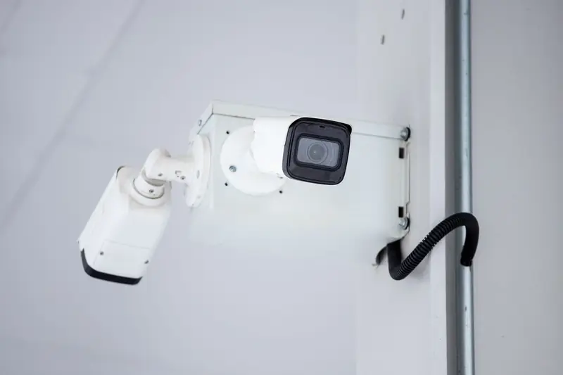 Deux caméras de vidéosurveillance fixées sur un mur clair du site.