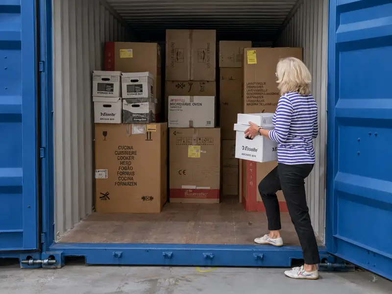 Une femme charge un carton dans un conteneur déjà rempli de cartons.