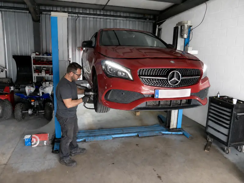 Une voiture levée sur un pont élévateur dans un garage loué, un homme au travail.